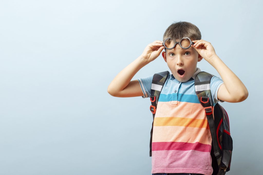Un enfant avec son cartable lève ses lunettes pour la photo scolaire