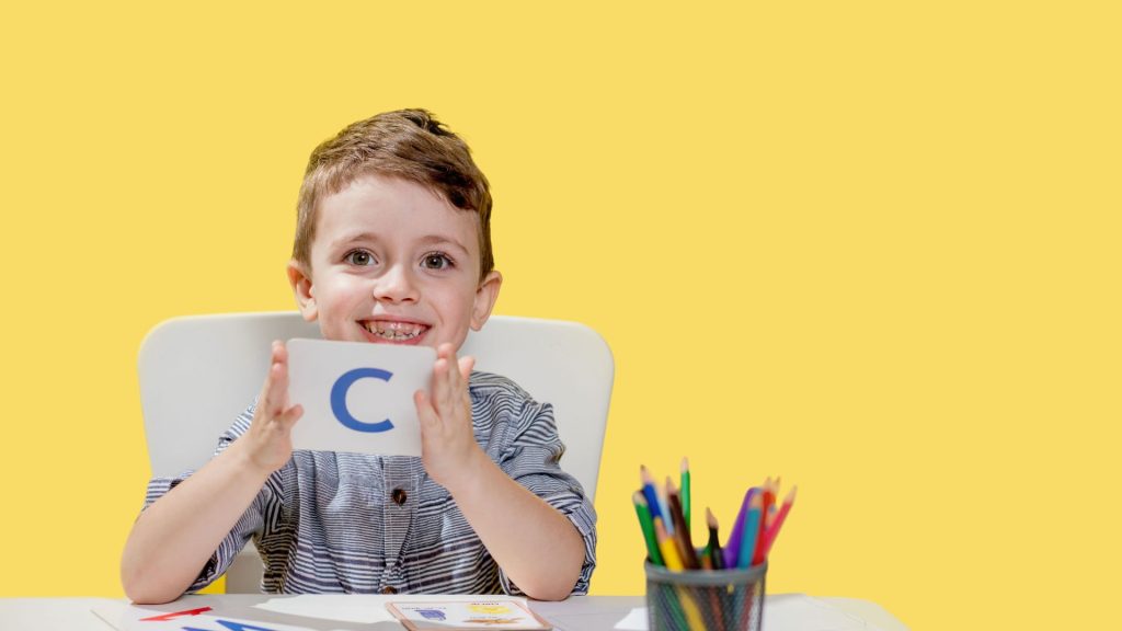 Une photo scolaire d'un élève tenant la première lettre de son prénom dans la main
