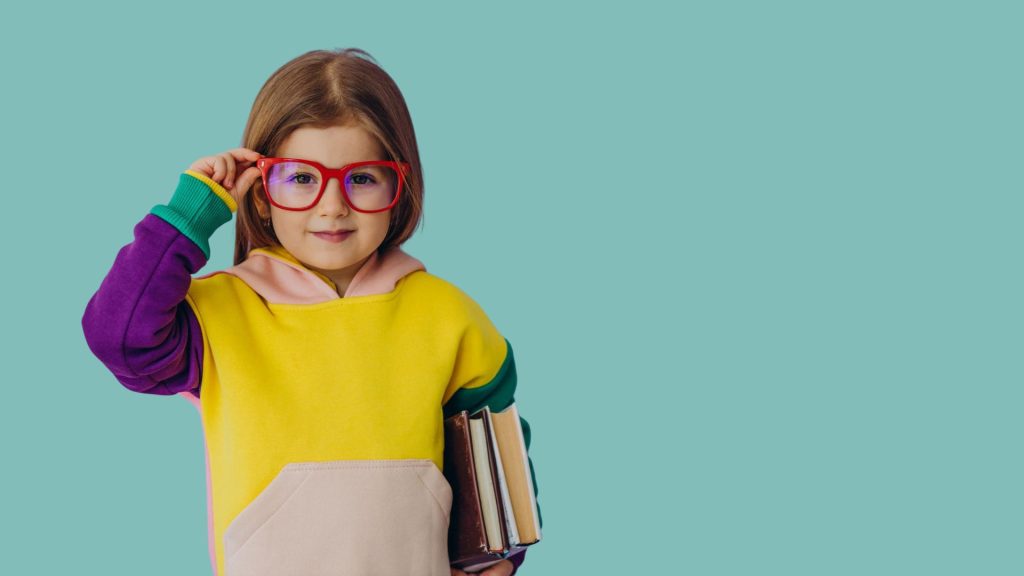 Une jeune enfant tient ses cahier dans une main et ses lunettes sur son nez dans l'autre